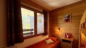 A cozy room with a single bed, a small table, and a window with curtains. - Apartment with station view - 2 guests (Valmorel)