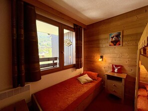 A cozy room with a single bed, a small table, and a window with curtains. - Apartment with station view - 2 guests (Valmorel)