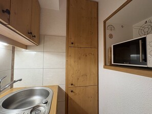 A kitchen with a stainless steel sink, wooden cabinets, and a microwave on the wall. - Apartment with station view - 2 guests (Valmorel)