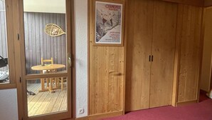 A room with a wooden door, a poster on the wall, and a view through a glass door. - Apartment with station view - 2 guests (Valmorel)