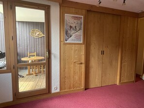 A room with a wooden door, a poster on the wall, and a view through a glass door. - Apartment with station view - 2 guests (Valmorel)