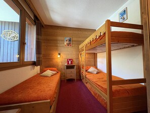 A room with two bunk beds, a small desk, a chair, a window with blinds, and a wall-mounted light fixture. - Apartment with station view - 2 guests (Valmorel)
