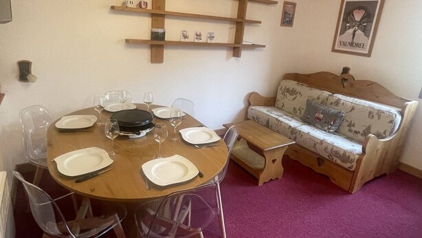 A dining area with a round table set for four, a sofa, and a wall-mounted shelf with decorative items. - Apartment with station view - 2 guests (Valmorel)