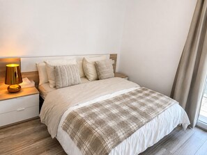 A neatly made bed with a plaid blanket, a bedside lamp, and a wooden nightstand. - Apartment with AC & WiFi - 3 guests near beach (Platja d'Aro)