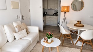 A modern living room with a sofa, a small round table with a potted plant, and a dining area with chairs and a table. - Apartment with AC & WiFi - 3 guests near beach (Platja d'Aro)