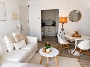 A modern living room with a sofa, a small round table with a potted plant, and a dining area with chairs and a table. - Apartment with AC & WiFi - 3 guests near beach (Platja d'Aro)