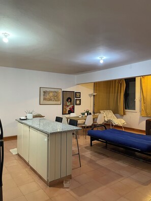 A compact living space with a kitchenette, a dining area, a bed, and a window with curtains. - Charming 1-bedroom apartment in Playa Juan Dolio near the beach (Playa Juan Dolio)