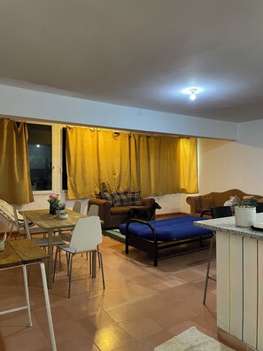 A living room with a sofa, a dining table with chairs, a bed, and a window with curtains. - Charming 1-bedroom apartment in Playa Juan Dolio near the beach (Playa Juan Dolio)