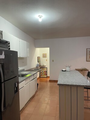A kitchen with white cabinets, a black refrigerator, a countertop with a sink, and a small island with a bar stool. - Charming 1-bedroom apartment in Playa Juan Dolio near the beach (Playa Juan Dolio)
