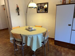 A dining area with a round table, chairs, a lamp, and a refrigerator. - Apartment with private garden - 6 guests (Port Camargue)