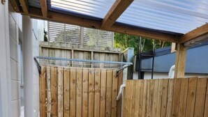 A covered outdoor area with a wooden fence, a bench, a table, and a hose. - Tranquil 1-bedroom apartment with AC in charming Whangārei (Whangārei)
