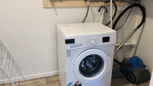 A compact laundry room with a front-loading washing machine, a hose reel, and a vacuum cleaner. - Tranquil 1-bedroom apartment with AC in charming Whangārei (Whangārei)