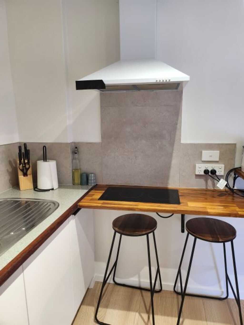 A compact kitchen with a built-in stove, two stools, and a white range hood.