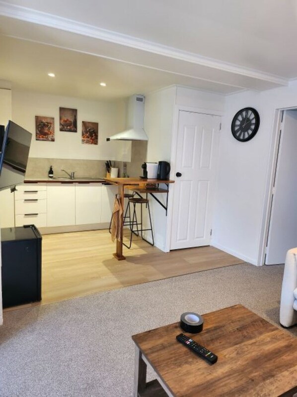A modern kitchen with white cabinets, a wooden countertop, and a built-in stove. There is a dining area with a wooden table and chairs, and a living room with a carpeted floor and a coffee table.