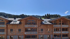 En træbygning med flere etager og altaner, sandsynligvis et hotel eller en hytte, med et bjerglandskab i baggrunden.