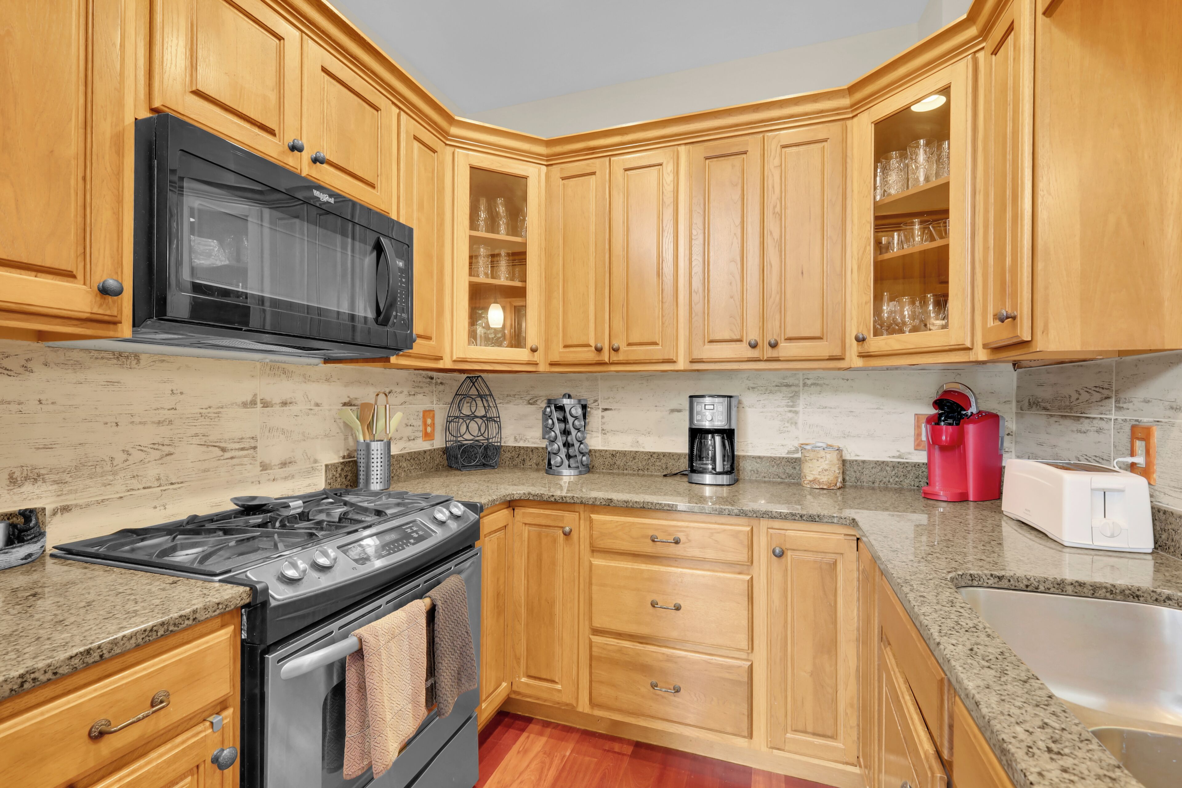 A kitchen with wooden cabinets, a black microwave, a coffee maker, and a toaster.