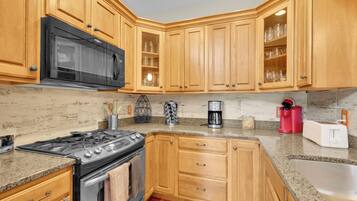 A kitchen with wooden cabinets, a black microwave, a coffee maker, and a toaster.