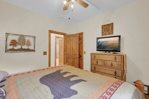 Ein Schlafzimmer mit einem Bett, einer Holzkommode, einem Fernseher und einer Tür zu einem anderen Raum.