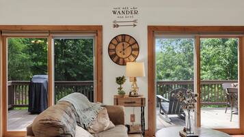 A cozy living room with a large wooden clock, a comfortable couch, and a view of a wooden deck through large glass doors.