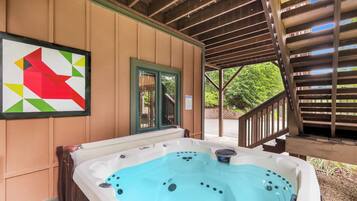 A hot tub under a wooden pergola with a view of a garden.
