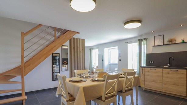 Un comedor con escalera de madera, una cocina con baldosas oscuras y vistas al exterior.