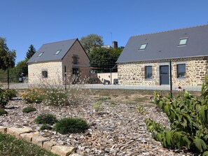 A stone building with a sloped roof and a fenced garden area with various plants. - Charming modern lodging - 6 guests (La Ferté-Macé)