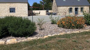 Un edificio de piedra con techo plano y un pequeño jardín con flores y arbustos.