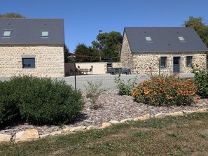 Ein Steinhaus mit flachem Dach und einem kleinen Garten mit Blumen und Sträuchern.
