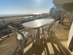 Een balkon met een tafel en stoelen, met uitzicht op een stadsbeeld en de oceaan.