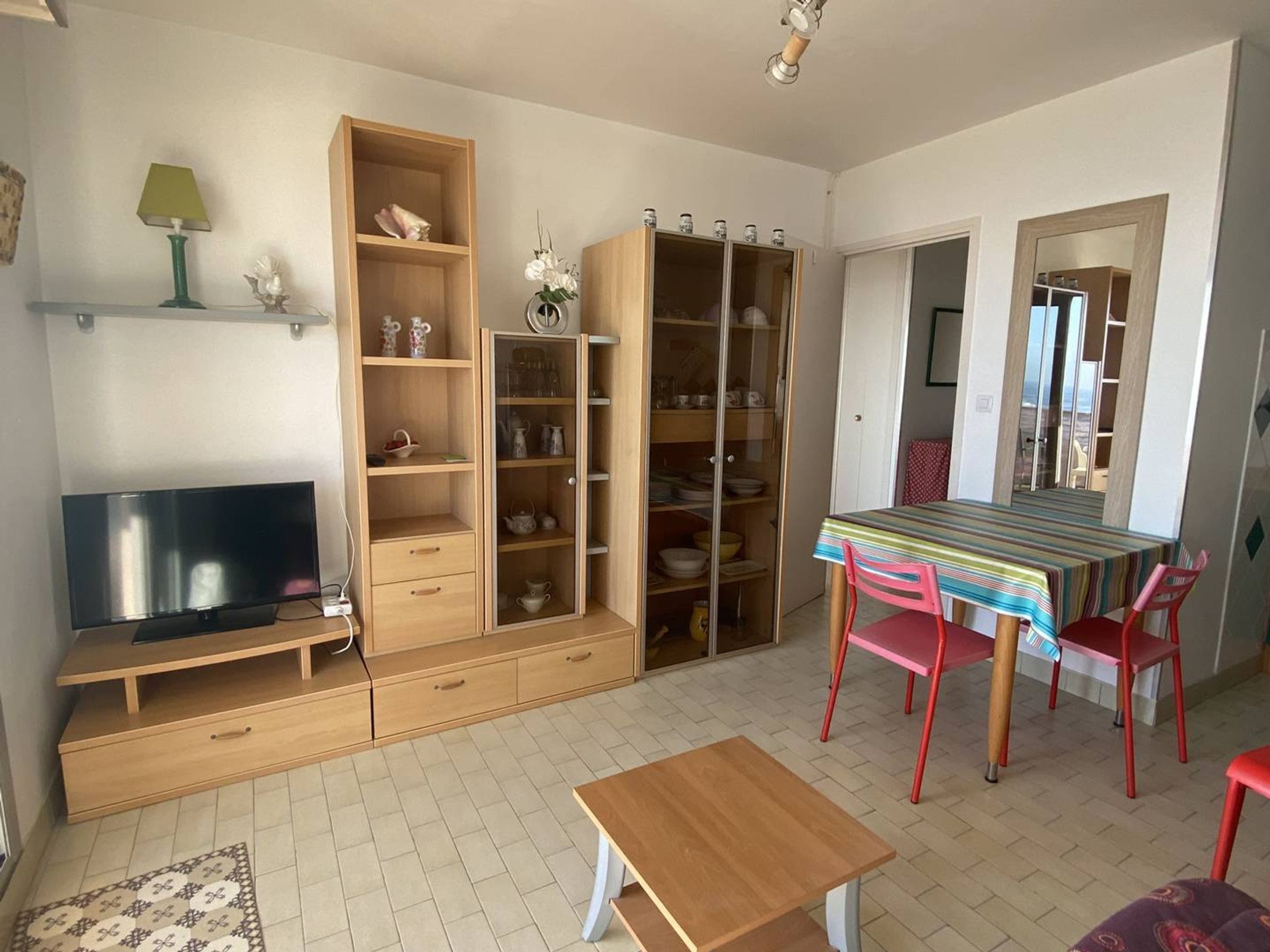 A compact living space with a television, wooden furniture, a dining table with chairs, and a patterned rug.
