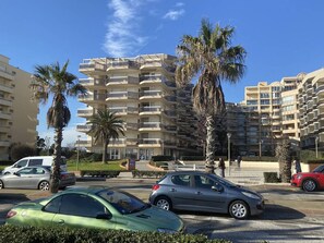 A multi-story residential building with balconies, palm trees, and parked cars. - Apartment with sea view terrace - 4 guests (Canet-Plage)