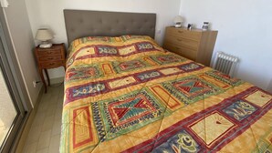A bedroom with a bed, a nightstand, a dresser, a radiator, and a framed picture on the wall. - Apartment with sea view terrace - 4 guests (Canet-Plage)