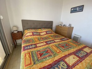 A bedroom with a bed, a nightstand, a dresser, a radiator, and a framed picture on the wall. - Apartment with sea view terrace - 4 guests (Canet-Plage)