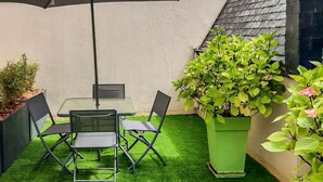 Un patio con una mesa, sillas, un paraguas grande y plantas en macetas.