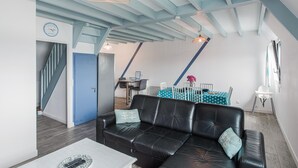 Una sala de estar moderna con un sofá de cuero negro, un comedor con mesa y sillas, y una escalera que lleva a otro nivel.