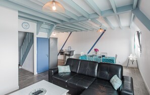 A modern living room with a black leather sofa, a dining area with a table and chairs, and a staircase leading to another level. - 2 bedroom gorgeous apartment in Lezardrieux (Lezardrieux)