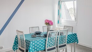 Un comedor con una mesa dispuesta para seis comensales, sillas blancas, mantel con estampado de estrellas en color verde azulado y un florero con flores rosas.