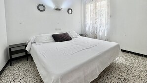 Ein Schlafzimmer mit einem Bett, einem Nachttisch, einer Wanduhr, einer Wand-Klimaanlage und einem Fenster mit durchsichtigen Vorhängen.
