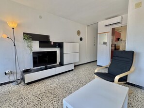 A modern living room with a flat-screen TV, a sofa, a coffee table, and a plant. - Apartment with AC and parking - 4 guests (Roses)