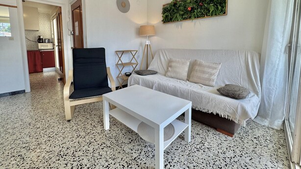 Ein Wohnzimmer mit Sofa, Sessel, Couchtisch, Lampe und einer Wandpflanze.