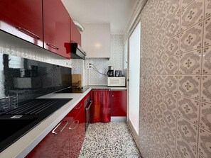 A compact kitchen with a black stove, red cabinets, and a microwave on the countertop. - Apartment with AC and parking - 4 guests (Roses)
