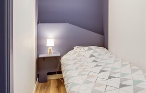 A small, narrow room with a bed, a nightstand, and a lamp. - 1 bedroom lovely apartment in Lezardrieux (Lezardrieux)