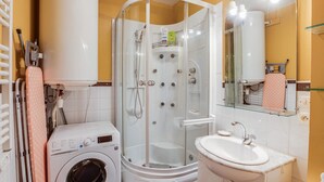 Ein Badezimmer mit Waschmaschine, Duschkabine, Waschbecken und Spiegel.