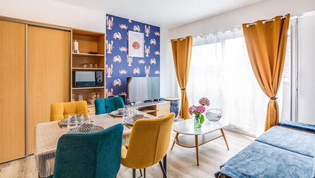 Ein modernes Wohnzimmer mit Essbereich, Fernseher und einem großen Fenster mit Vorhängen.