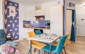 A modern kitchen with white cabinets, a blue backsplash, and a dining area with a table set for four. - 1 bedroom lovely apartment in Lezardrieux (Lezardrieux)