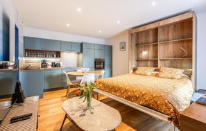 A modern hotel room with a bed, a dining table, a kitchen area, and a small balcony. - Apartment in Lezardrieux (891) (Lezardrieux)