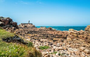Un paysage côtier rocheux avec un phare, un ciel bleu dégagé et une mer calme.