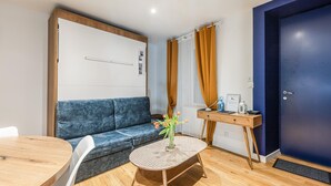Quarto moderno com sofá azul, mesa redonda e pequena mesa lateral com um vaso de flores.