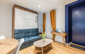A modern room with a blue sofa, a round table, and a small side table with a vase of flowers. - Apartment in Lezardrieux (891) (Lezardrieux)