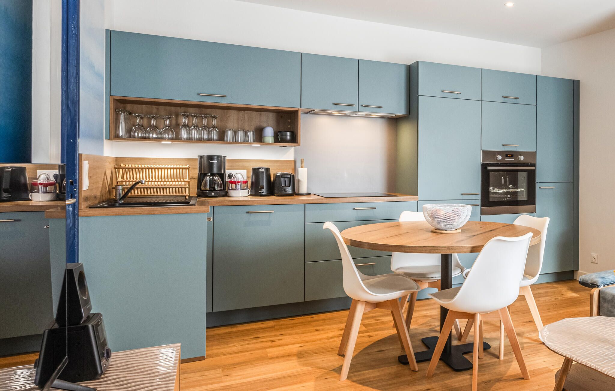 Eine moderne Küche mit blauen Schränken, einem runden Holztisch und weißen Stühlen.